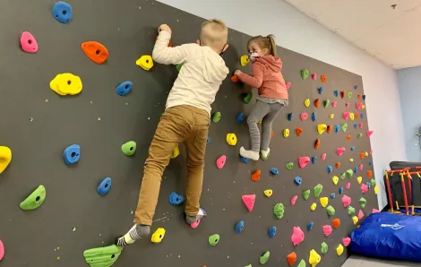 Two young kids wearing masks climb on an indoor climbing wall at Kaleidoscope Family Gym indoor play gym in Puyallup, Wash.