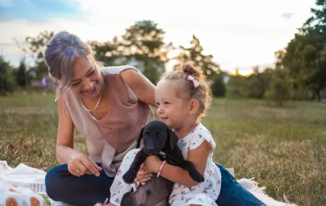 mother and daughter on a picnic blanket outside with a cute black puppy