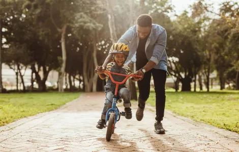 black dad pushing his smiling son on a bike