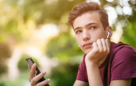 boy outdoors holding a cell phone with a serious look on his face
