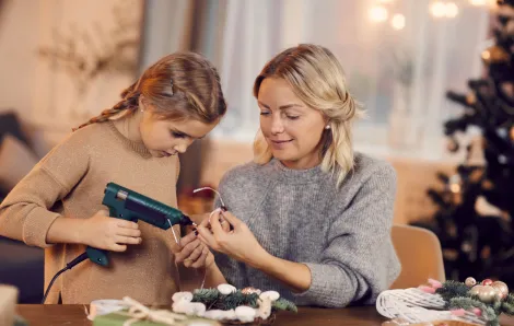 mother and daughter doing a craft with a hot glue gun with a christmas tree in the background