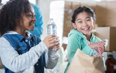 two kids filling paper bags with water bottles and canned goods