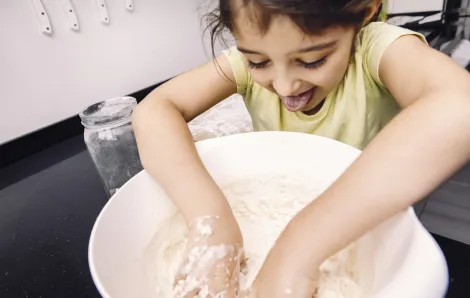 Cute little girl sticks her tongue out as she mixes flour in a bowl 