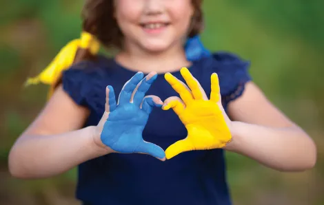 Child with one hand painted blue, the other yellow, holding them up to make a heart with their fingers.