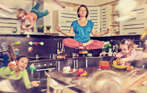 Mother meditating in her kitchen as her three children fly around the room