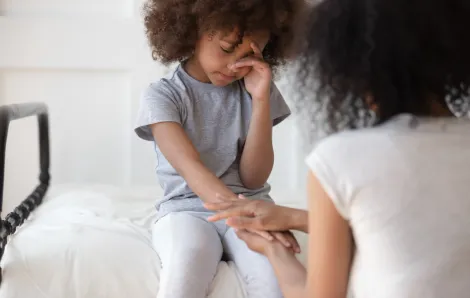 Girl sitting on a bed looking sad, mom holding her hand