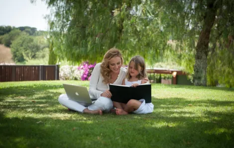 Jessica Joelle Alexander, and her daughter Sophie, sitting in the grass with a book and a computer