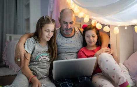 Dad watching tv on a computer with two daughters 