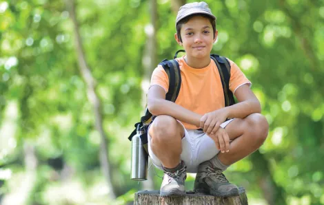 Boy sitting on a rock in the forest at a one-day or drop in Summer camp 