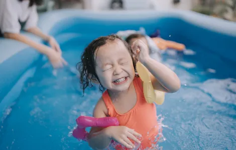 Child smiles while playing in an inflatable pool.
