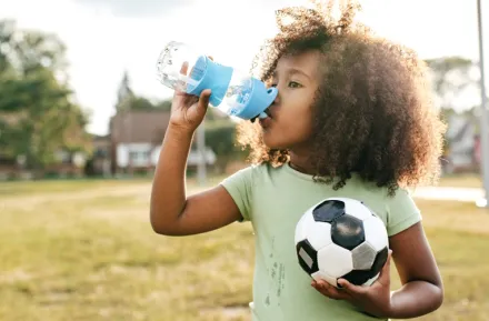 Young girl holding a soccer ball and drinking water at a sports camp in Seattle