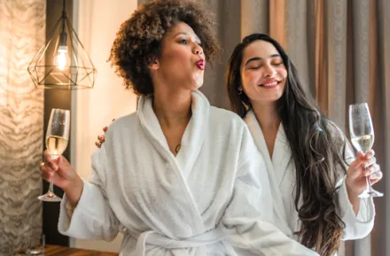 Two female friends relaxing in white robes holding champagne, credit iStock