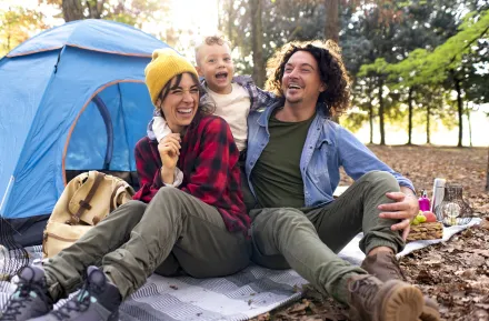 A couple and their young child laughing in front of their tent while camping.
