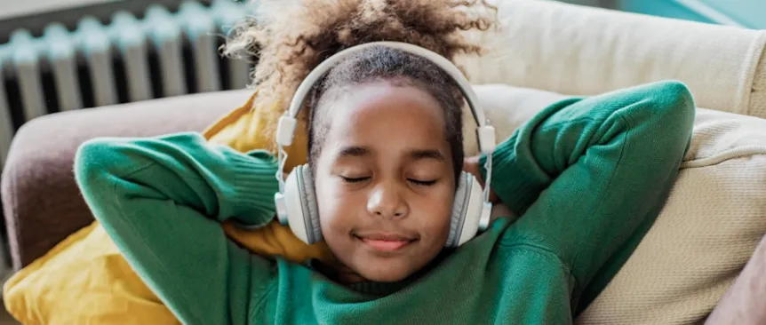 Young girl lying on a couch with eyes closed wearing headphones listening to a best podcasts for kids