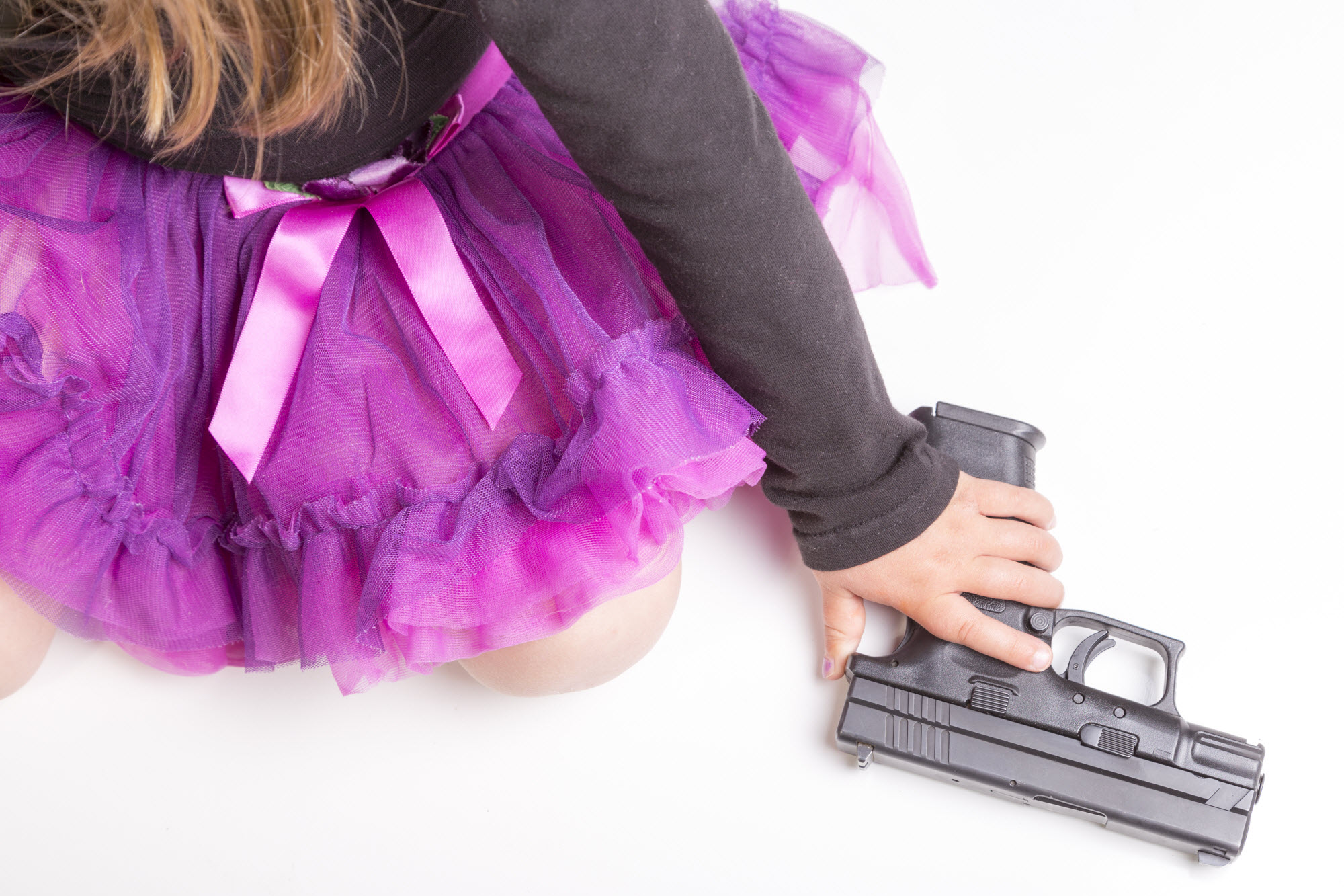 little girl in purple pink skirt grabbing a gun from the floor
