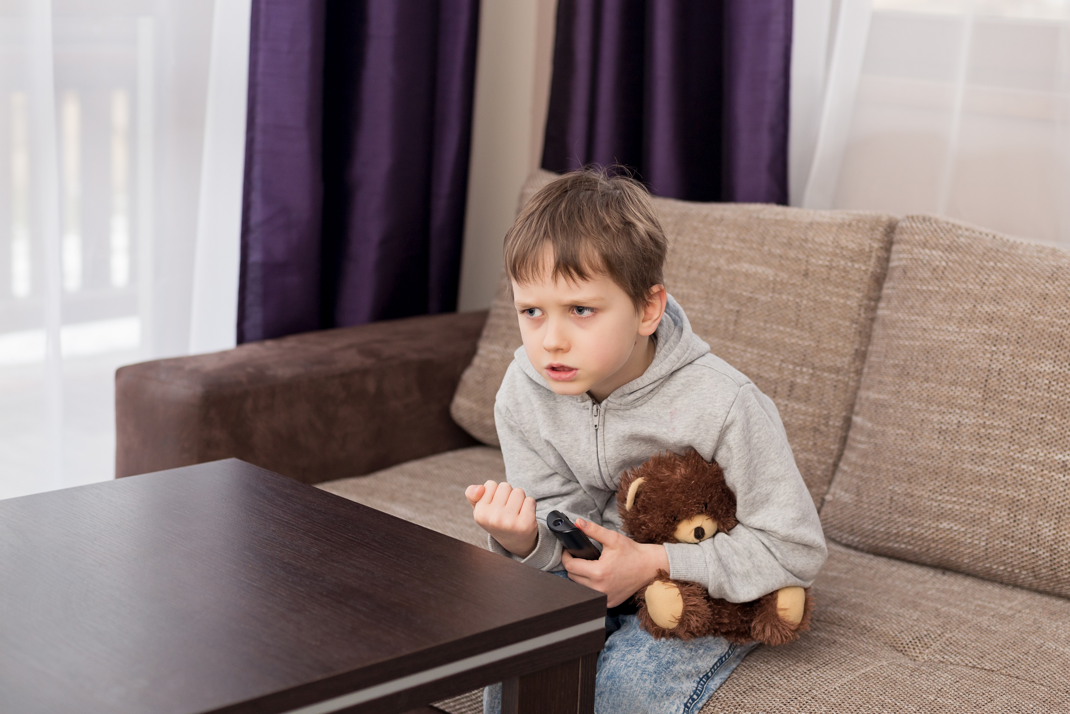 Little boy holding teddy bear and watching TV, looking stressed