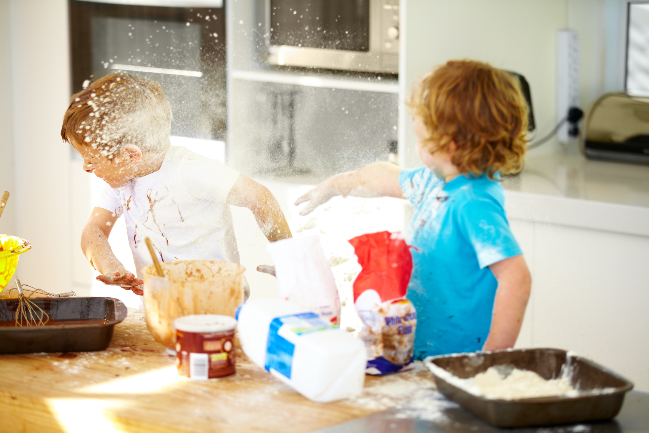 Kid throwing flour at another kid in the kitchen