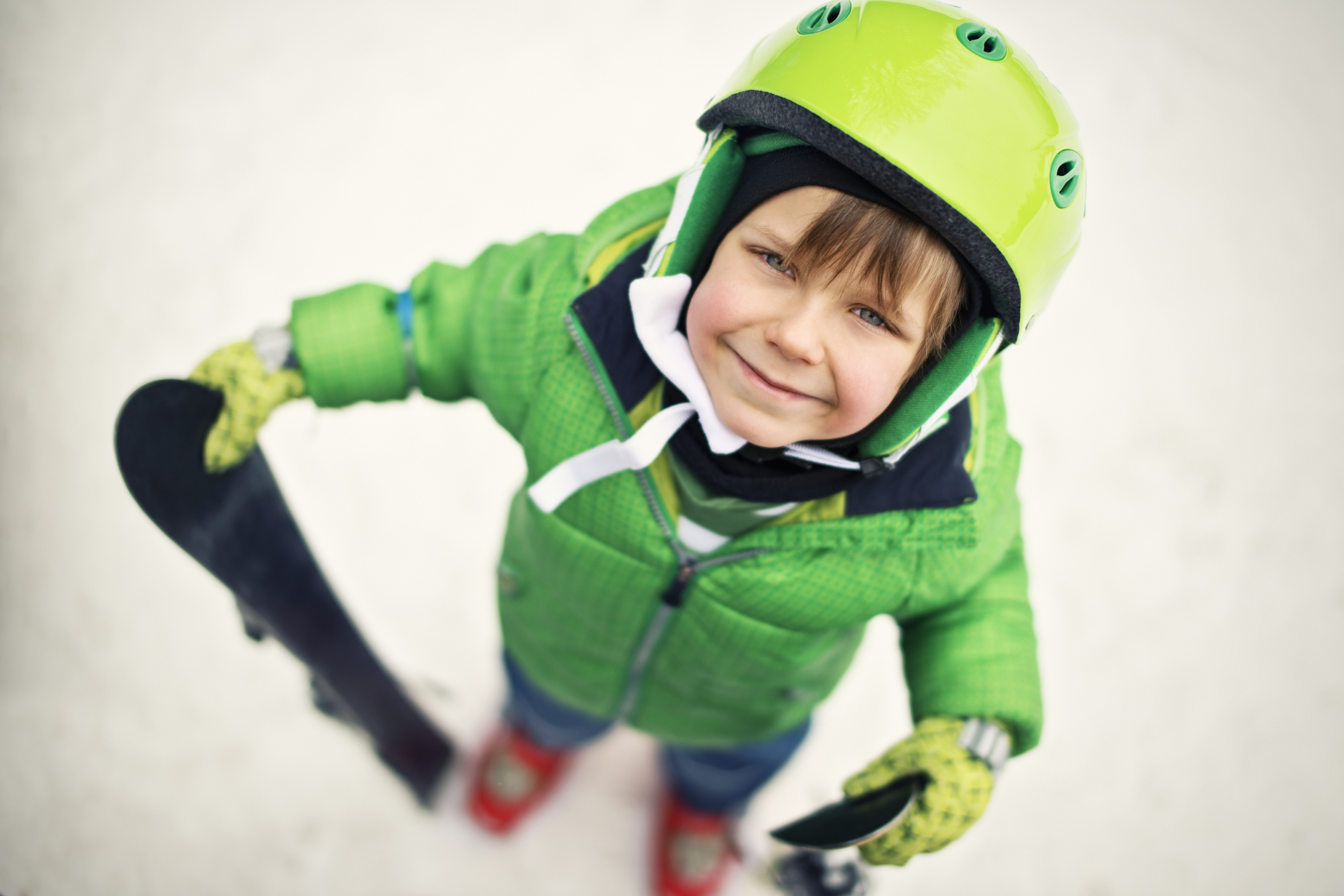 Kid with helmet and skis looking up at camera