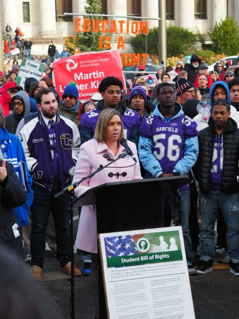 Summer Stinson speaking at a rally on MLK Day 2017 on the steps of the Washington state capitol with the Garfield Football Team behind her. 