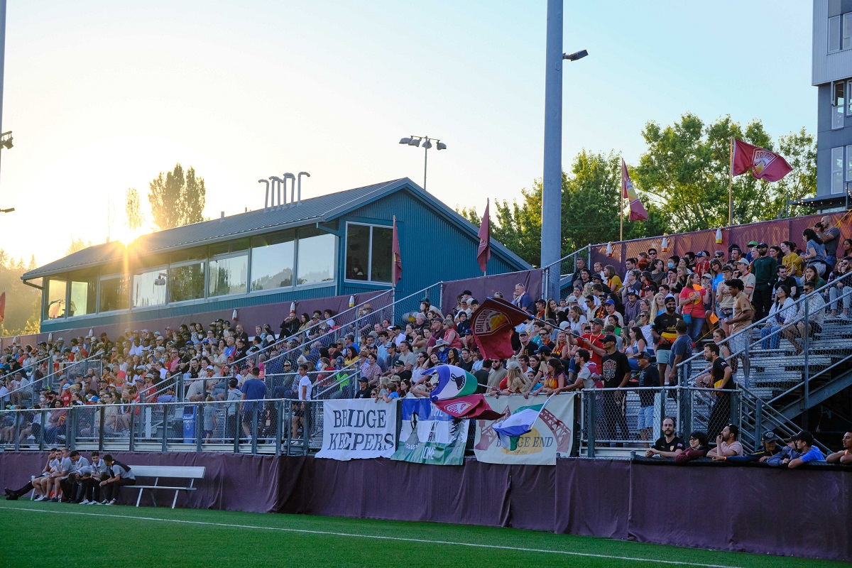 Fans in the stands watch a Ballard FC match during the 2022 season the sun is setting behind