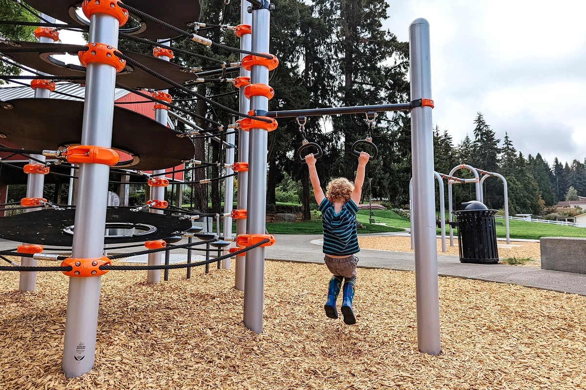 Small boy swings from rings at the new playground at Chestnut Ridge Park in Kent near Seattle