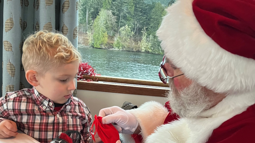 "Young boy sitting next to Santa looking at a small red bag on a Coco cruise at Alderbrook Resprt"
