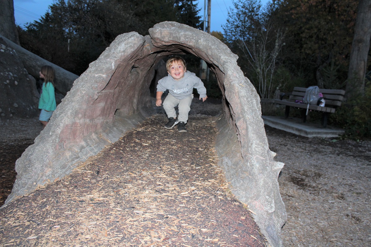 A young smiling boy runs through a tunnel at Discovery Bay play area at Tacoma Nature Center