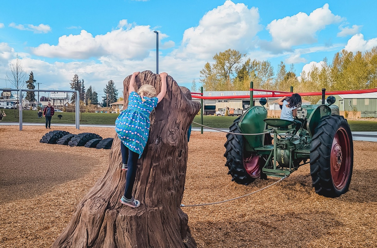 A girl climbs on the stump behind the real tractor at the new playground at Edgewood Community Park