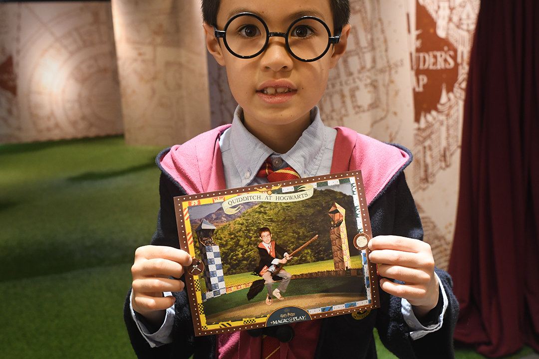 At Harry Potter: Magic at Play in Seattle a boy holds a photo of himself, on a Quidditch broomstick