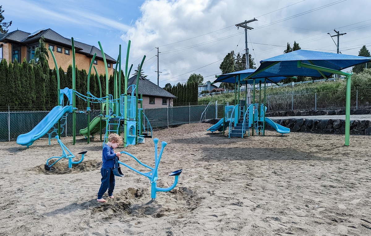 Little boy plays on with a sand digging machine play feature at the new playground at Renton's Kennydale Beach Park near Seattle along Lake Washington