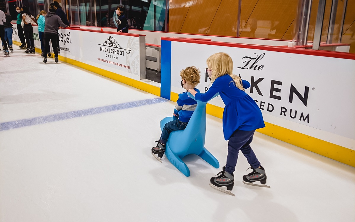 A little girl pushes her younger brother on a Bobby the Seal skate aid at Kraken Community Iceplex in Seattle, Wash, training home of the NHL Seattle Kraken