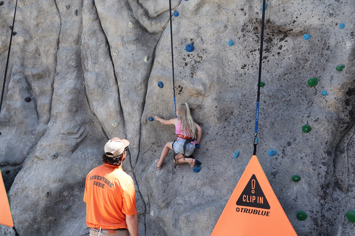 A girl tries out the rock climbing wall at the newly opened Leavenworth Adventure Park with a staff member watching over