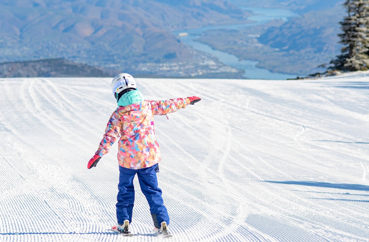Young skier on groomed run at Mission Ridge Ski and Snowboard Resort with town of Wenatchee visible in the distance