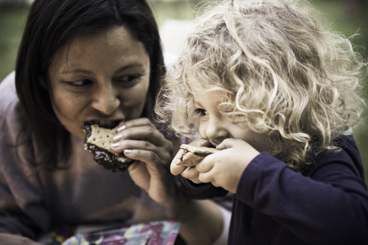 Close-up view of a mom and a child eating s'mores they are camping in their backyard and having fun during a Seattle summer