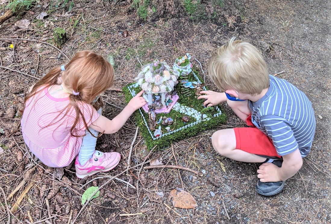 Two young kids crouch over and inspect a fairy house on the Pine Lake fairy trail in Sammamish, Washington, near Seattle, among best free summer activities for Seattle kids and families