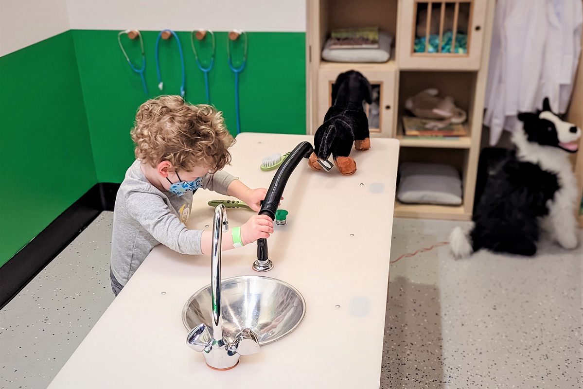 Young child plays with the features of the new Neighborhood Paws vet clinic exhibit at the reopened Seattle Children's Museum