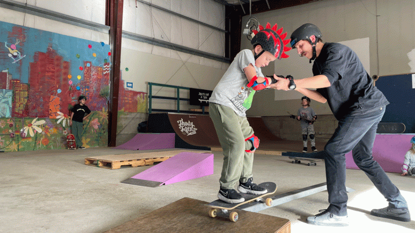 Young boy receiving skate boarding lessons from a skateboarding instructor