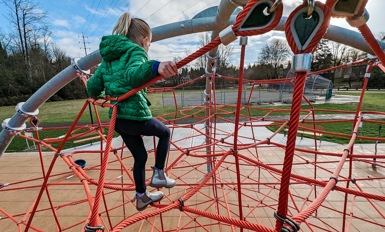 A girl sits atop the large rope dome climber at the new playground at the South Seattle area's Skyway Park