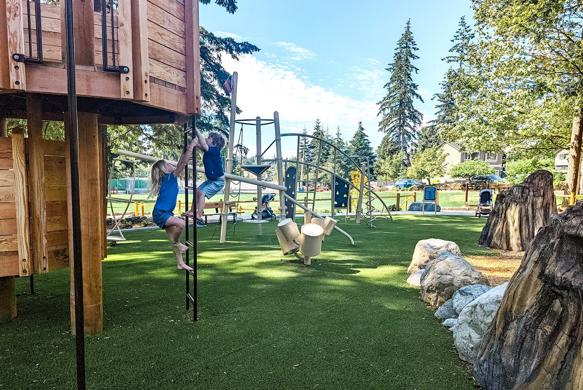 Two young kids climb opposite sides of a ladder reaching a two-story playhouse at South Lynnwood Park’s new playground, near Seattle