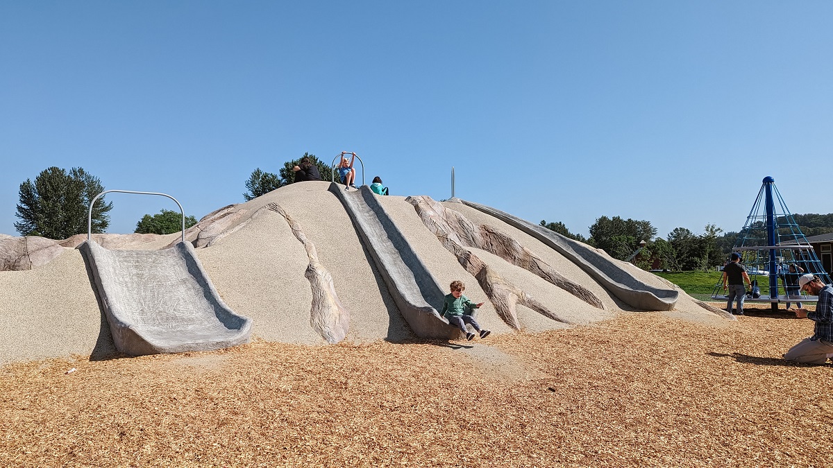 Kids descend the play mountain on slides at the new playground at Van Doren’s Landing Park in Kent, near Seattle