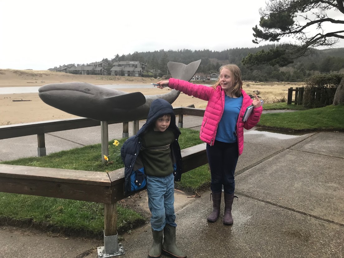 A young brother and sister pose in front of the whale sculpture at Whale Park in Cannon Beach, Oregon.
