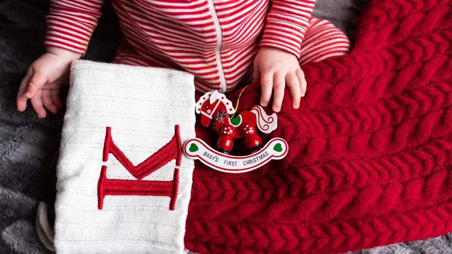 "Baby in white and red striped pajamas next to a Christmas stocking and ornament"
