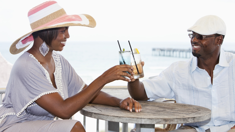 "A couple toasting with drinks at a small table near the beach on a kid-free vacation"