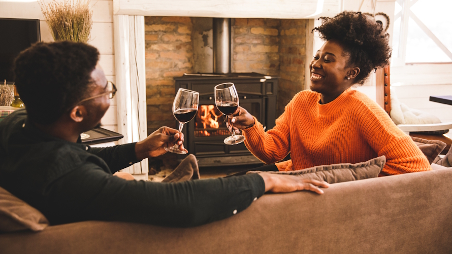 "Couple sitting on a couch with glasses of wine in front of a fireplace"