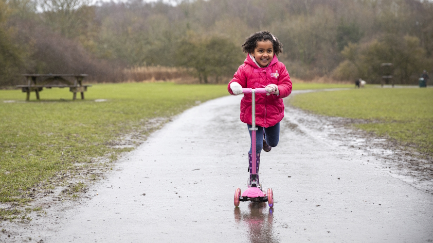 "Young girl riding a scooter in the rain"