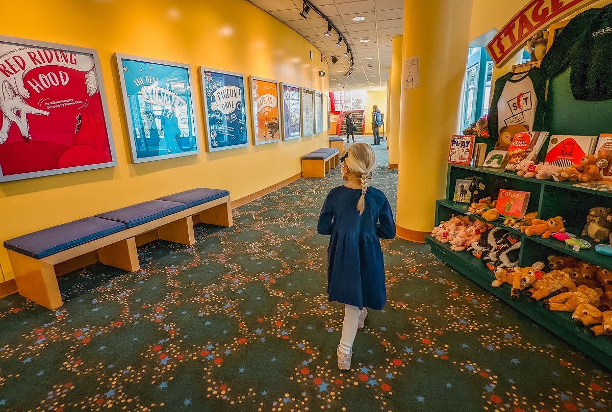 A girl in a blue dress walks away in the lobby of Seattle Children's Theatre 