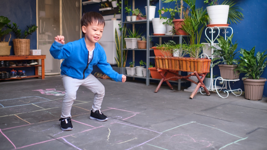"Young child hoping on a hopscotch course in a family competition based on a tv show"