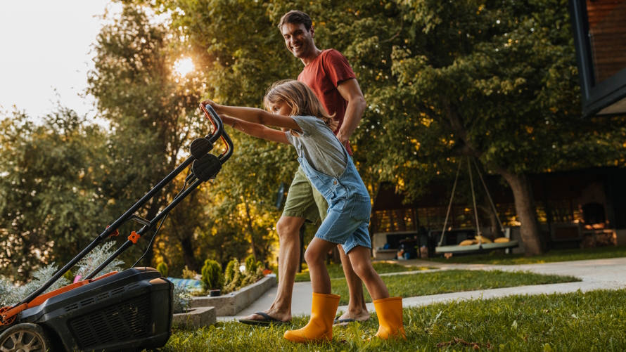 "Young girl mowing the lawn with an adult watching"