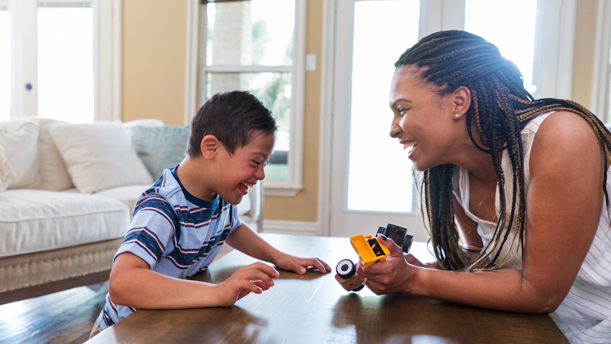 "Mom and child sitting at a coffee table laughing and playing with toy cars"