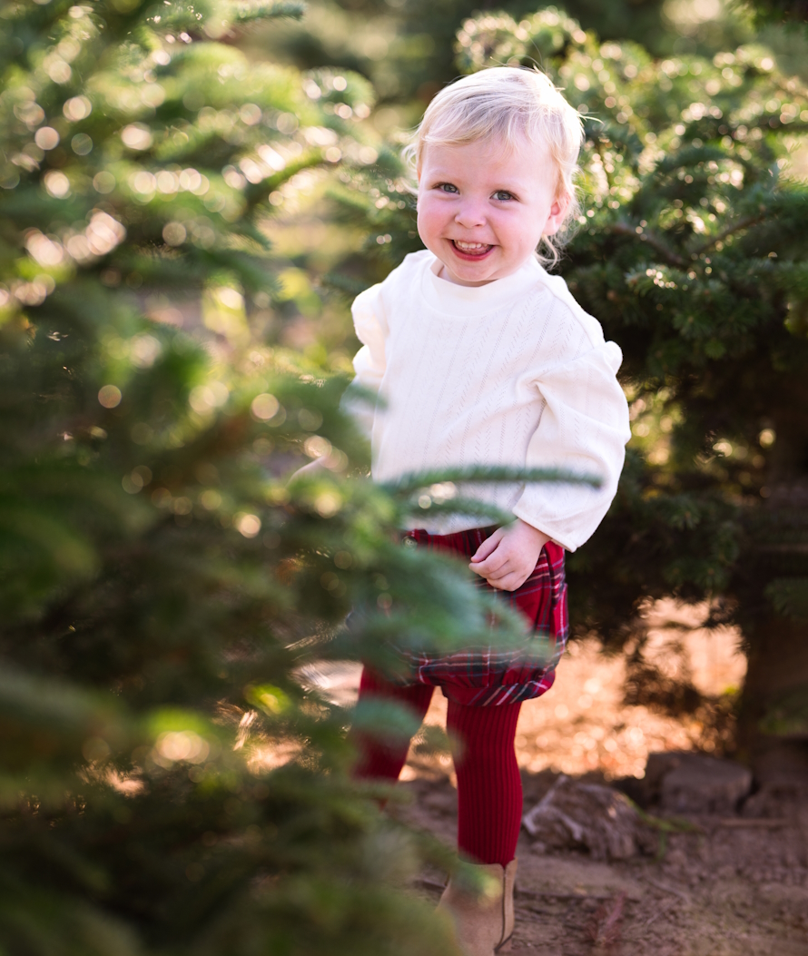 "Young girl standing next to Christmas trees outside"